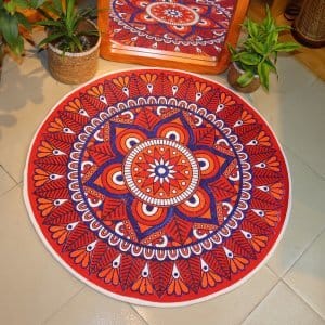 Handwoven round jute and cotton floor mat with colorful mandala design placed on tiled floor, surrounded by woven baskets and green plants