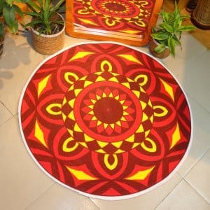 Handwoven round jute and cotton floor mat with colorful mandala design placed on tiled floor, surrounded by woven baskets and green plants