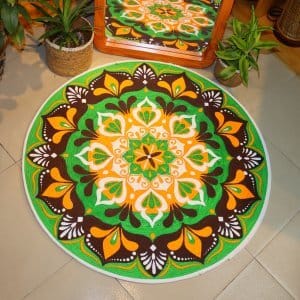 Handwoven round jute and cotton floor mat with colorful mandala design placed on tiled floor, surrounded by woven baskets and green plants