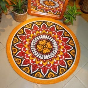 Handwoven round jute and cotton floor mat with colorful mandala design placed on tiled floor, surrounded by woven baskets and green plants
